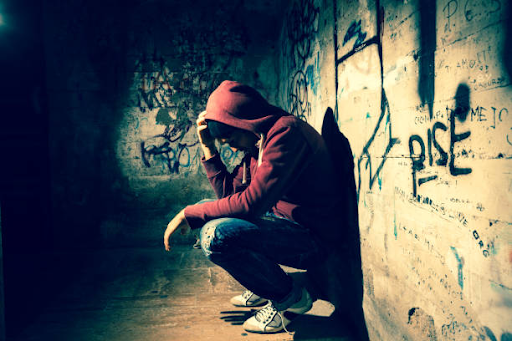 A person sitting alone with their head down in a dimly lit urban setting, conveying emotional distress and the impact of addiction.