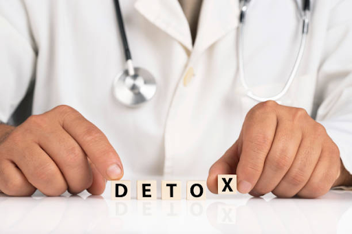 Doctor arranging wooden letter blocks spelling "DETOX" on a table, with a stethoscope around their neck, representing medical detoxification or supervised detox treatment.
