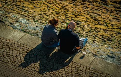 Two people sitting together on stone steps outdoors, seen from above, each with a takeaway coffee cup beside them.