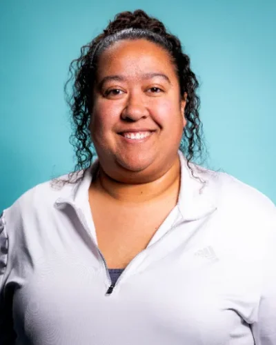 Destini Arbogast, therapist at HAWC Recovery, smiling against a teal background, showcasing a supportive and approachable demeanor.