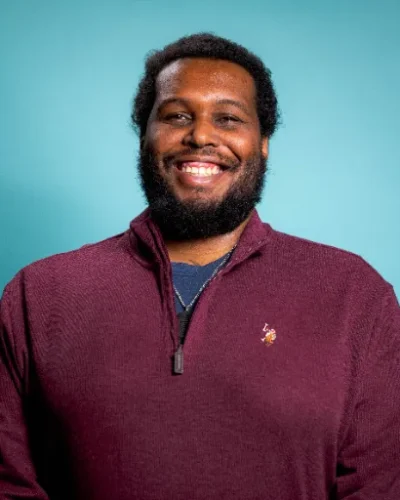 Kyron Cooper, Behavioral Health Tech at HAWC Recovery, smiling against a teal background, representing the supportive staff dedicated to client recovery.