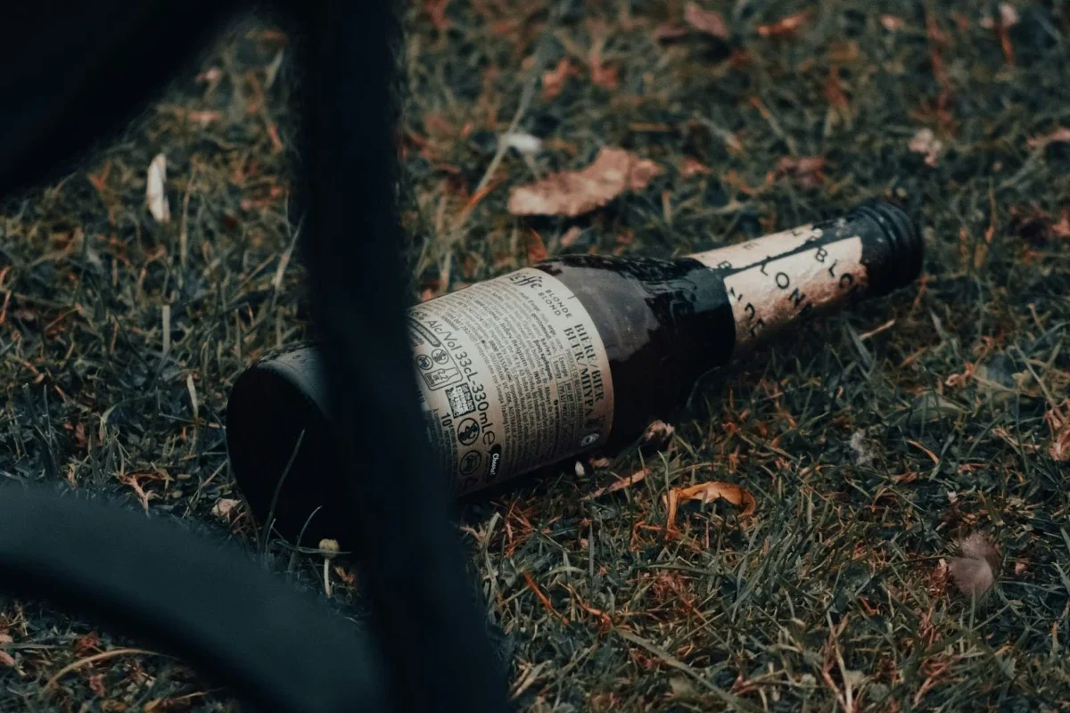 A discarded beer bottle lying on its side in dry grass, symbolizing substance use and addiction