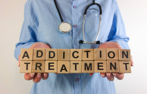 Healthcare professional holding wooden blocks spelling &ldquo;Addiction Treatment&rdquo; with a stethoscope around their neck
