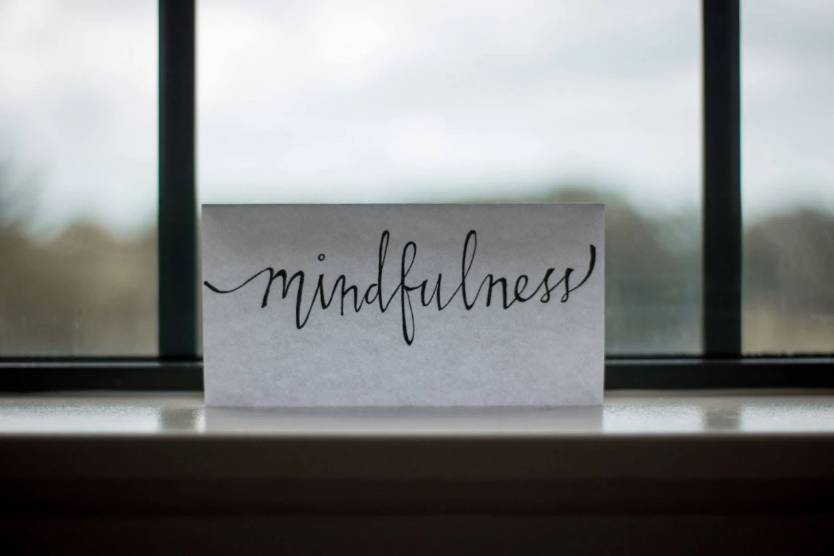 A small white card with the word "mindfulness" written in cursive calligraphy, propped on a windowsill.