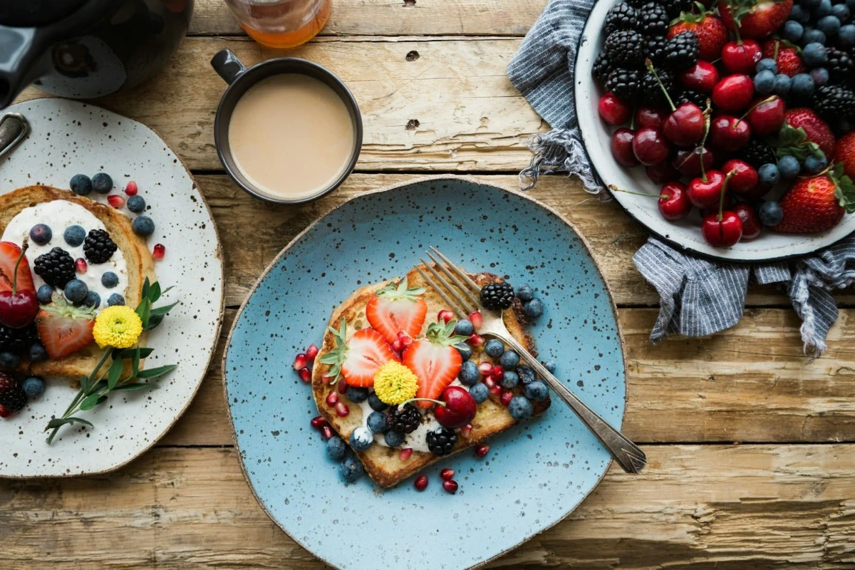 Overhead view of two plates of French toast topped with fresh mixed berries on a rustic wooden table.